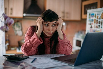 Sad woman holding her head over utility bills in front of a laptop. The concept of rising prices...