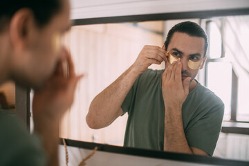 Spa day at home. Young man with patches under his eyes at the mirror at home.