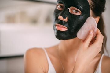 A beautiful brunette woman makes facial skin care procedures with a cleansing, moisturizing mask near the mirror in a bright room