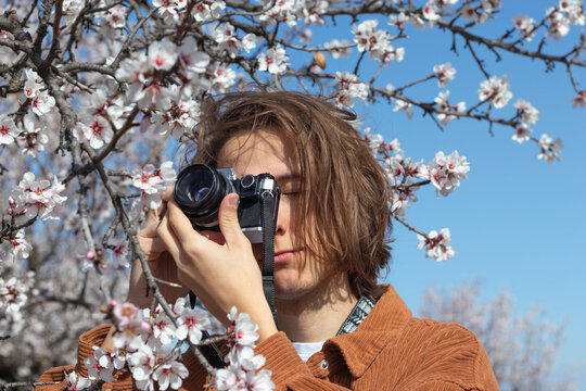 Portrait of young long haired man taking pictures with a film camera flowers