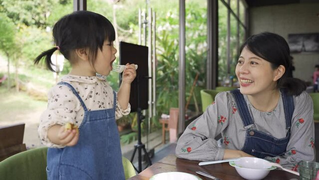 happy asian mother and child girl in matching outfit having good time talking and smiling while eating lunch in a cozy bright caf&eacute; restaurant