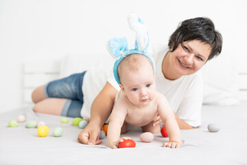 Obraz na płótnie Canvas Mother and child with colorful eggs. Mom and baby with bunny ears. Parent and kid play indoors in spring. Family celebrating Easter