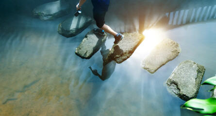 Man across stepping stones to cross a stream - Powered by Adobe