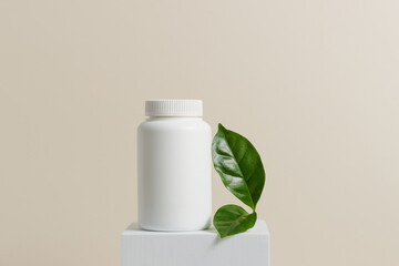 Mockup container for pills, capsules and vitamins on white stand with green leaf. White bottle with...