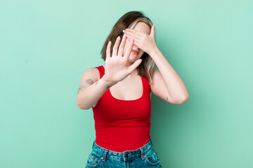 pretty caucasian woman covering face with hand and putting other hand up front to stop camera,...