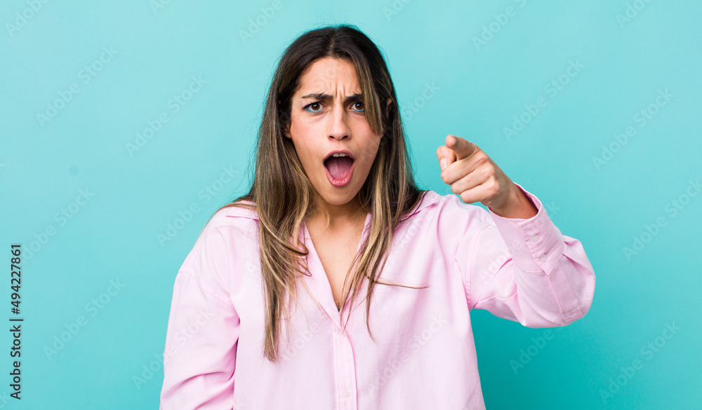 Wall mural pretty hispanic woman pointing at camera with an angry aggressive expression looking like a furious,