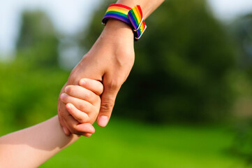 parent holds the hand of a small child. mother holding baby's hand. rainbow lgbt bracelet on...
