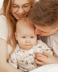 Portrait of cheerful smiling cozy and married couple. Woman in glasses, man, baby. Protection and support kid in family