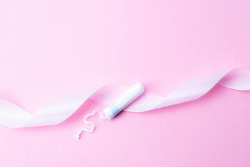 Tampon woman feminine hygiene. Pink ribbon with menstrual tampon on pink background. Menstruation feminine period. Soft tender protection for women critical days.
