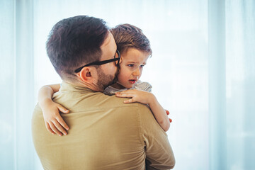 Father comforting stressed sad son. Close up of  father consoling his small sad son at home. Small boy crying in his father's hug at home.