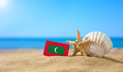 Fototapeta na wymiar Tropical beach with seashells and Maldives flag. The concept of a paradise vacation on the beaches of Maldives.