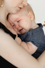 Face of crying child. Mother caring, holding wailing depressed baby in arms. Temperature, illness, kid colic. Close up