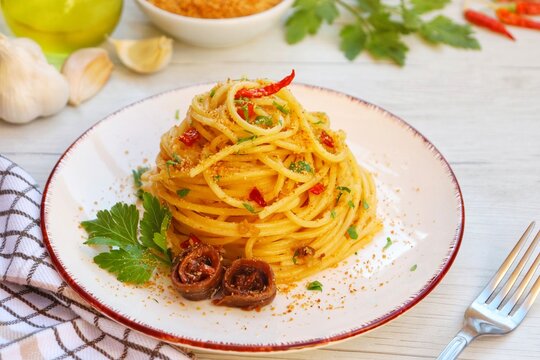 Italian Traditional Dish"Spaghetti con acciughe e pangrattato",spaghetti with anchovy,roasted breaf crumbs,garlics,olive oil,chilli peppers and parleys on plate with white wood background.Copy space
