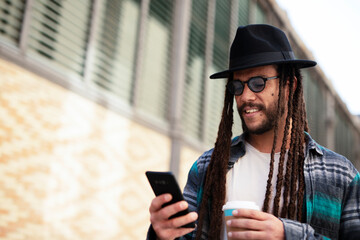 Handsome guy drinking coffee while walking in the street. Modern fashion man using the phone