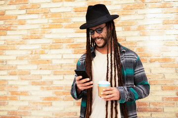 Handsome guy drinking coffee while walking in the street. Modern fashion man using the phone