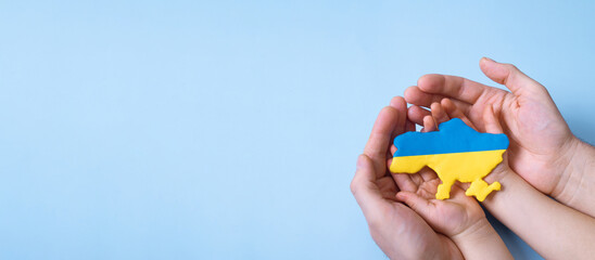 Shape of the map of Ukraine in yellow and blue colors in the hands of an adult and a child. Banner...