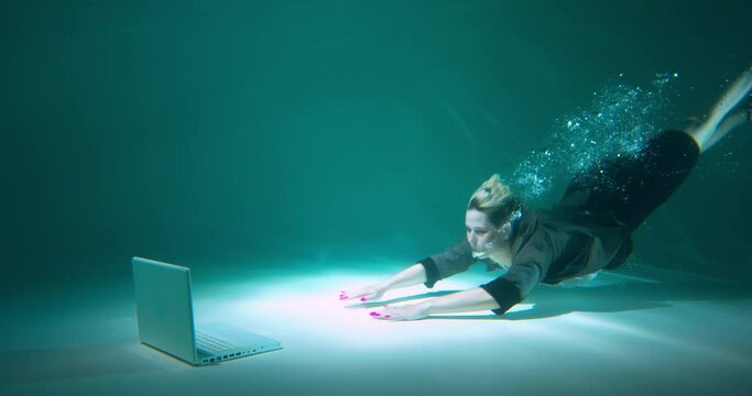 Beautiful happy young determined manager business woman dives underwater to work with laptop, cinematic slow motion.
