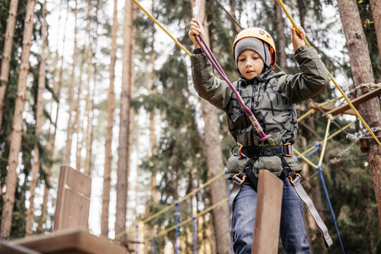Teenager boy in safety equipment routing and climbing in adventure rope park. Child in helmet climbing trees in an extreme park. Outdoor activities. Active lifestyle