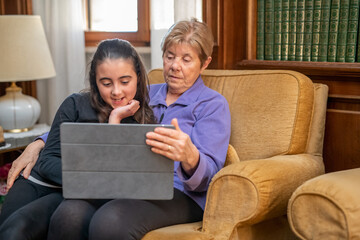 Little girl relaxes watching tablet in living room with grandmother.