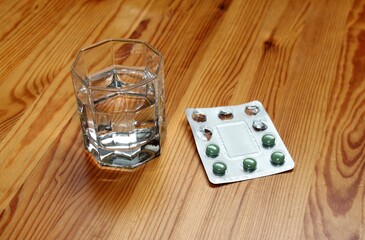 a glass of water with a blister pack of medicine with green tablets on a wooden table