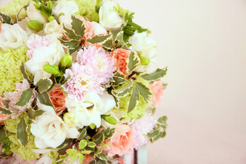 Round bouquet with white freesia flower, green dianthus, peach roses, light chrysanthemum and fresh greens. Bridal bouquet and wood on pink background. Front view, closeup