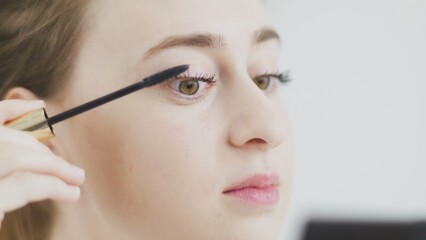 Make-up on the face. Close-up of a young woman painting her long eyelashes with black mascara.
