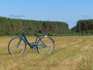 Fototapeta premium Bicycle on a mowed meadow against the backdrop of a pine forest on a clear day in the countryside; Russia, Ryazan Region - July 2021