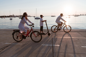 Happy family enjoying a beautiful morning by the sea together, parents riding a bike and their son riding an electric scooter. Selective focus 