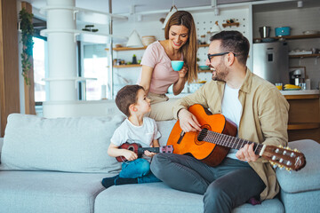 Father teaching his son to play on guitar at home. Son play on ukulele - hawaiian guitar. Father is teaching his 5 year old son to play guitar. First guitar class