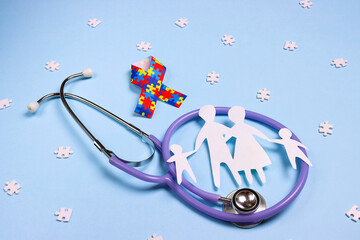 Autism concept with puzzle awareness ribbon, stethoscope and family paper silhouette on a blue background.