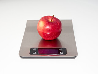 Red, fresh apple with water drops on the kitchen scale. White background.