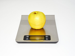 Yellow, fresh apple with water drops on the kitchen scale. White background.