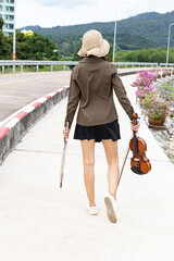 Beautiful asian woman hold violin ,flute walk on street nature view background ,in emotion feeling happy.