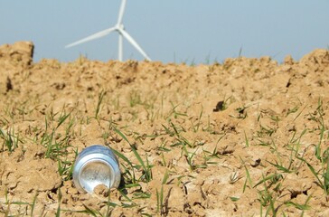 Canette en aluminium polluant la terre d'un champ avec une éolienne à l'arrière-plan