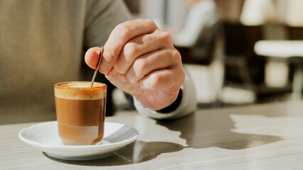 man stirs his machiatto with a coffee spoon