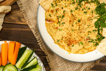 Partial view of a bowl with homemade Hummus with rackers and in another bowl carrots and other vegetables. Fresh, healthy and natural food concept. Copy space.