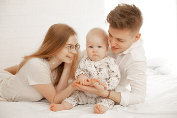 Happy joyful satisfied family of woman, man and infant baby lying in white bedspread. Family day together on vacation 