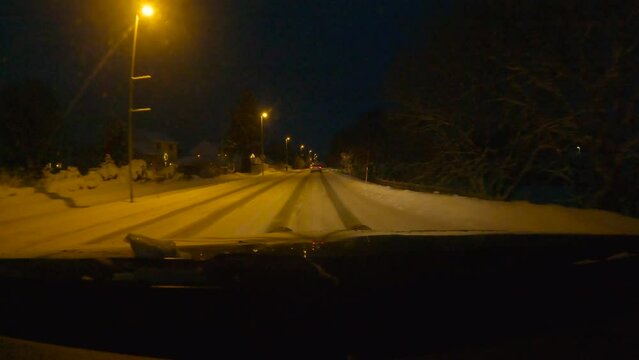 driving Sortland Norway city at night, on deep snowy and icy road with yellow orange street lights houses and traffic, Christmas