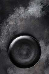Black plate on textured black background. vertical image. top view. place for text