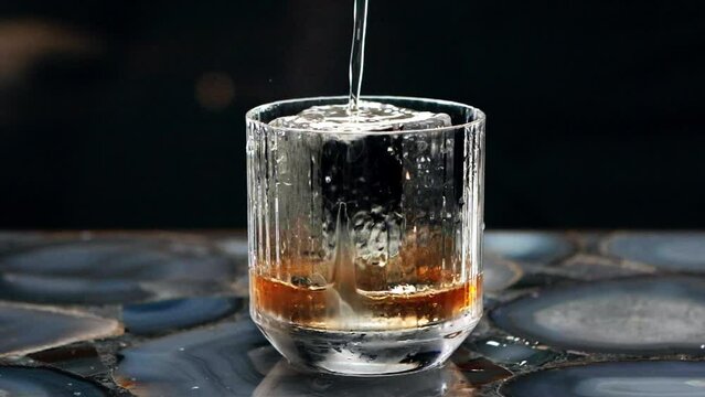 Close up of a professional bartender is preparing an alcoholic cocktail with professional crystal long lasting ice cubes to customers at the bar or disco club.

