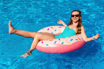young woman in bikini swims on the inflatable water donut in the swimming pool.