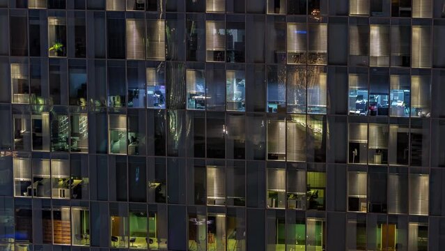 Night aerial view of office building glass window facade with illuminated lighted workspace rooms timelapse.