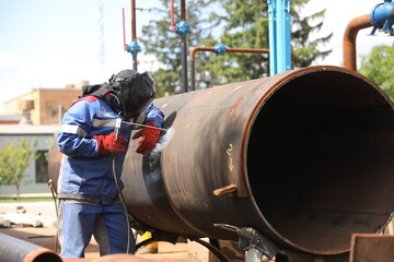 Male welder works. Welding joint of large diameter pipe. High pressure pipe welding for a gas station.