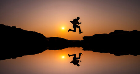 Fototapeta na wymiar silhouette of a man jumping on a rock reflection on water,Vivid sunset sky.