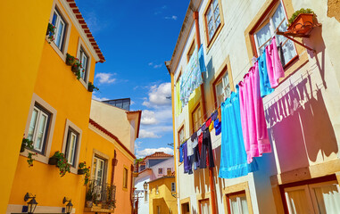 Fototapeta na wymiar Lisbon, Portugal. Antique Alfama district with coloured houses on background of blue sky with clouds. Washed linen dry on ropes on streets between building. Decorative street lamp on the wall.