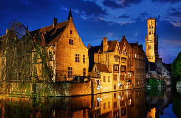Naklejka premium Bruges, Belgium. Evening sunset with blue sky. Water channels of ancient medieval town with view to Belfort van Brugge tower, famous landmark.