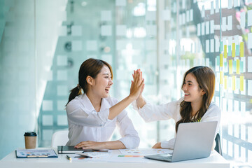 Young asian business woman giving high five with friends while working with computer laptop at office.