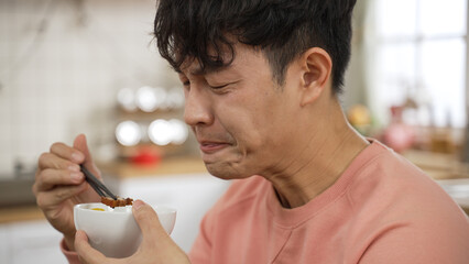 asian Japanese man making funny face expression while tasting spicy hot food at dining table.