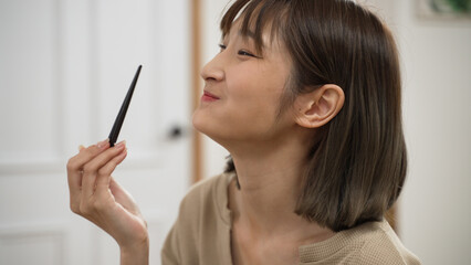 Obraz premium closeup portrait of a happy asian woman enjoying delicious food with chopsticks and bowl during dinner at home. she smiles with happiness while eating