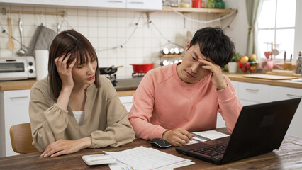 worried Asian husband and wife examining tax bills and calculating spending with a calculator at...